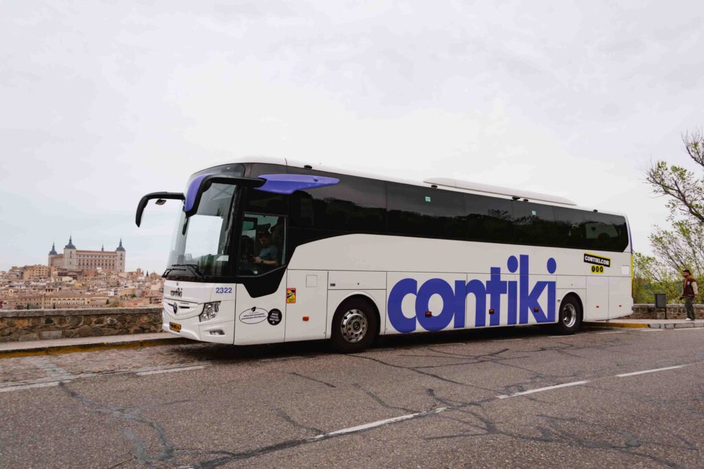 Large coach bus with Contiki brand name on the side with Toledo, Spain in the background