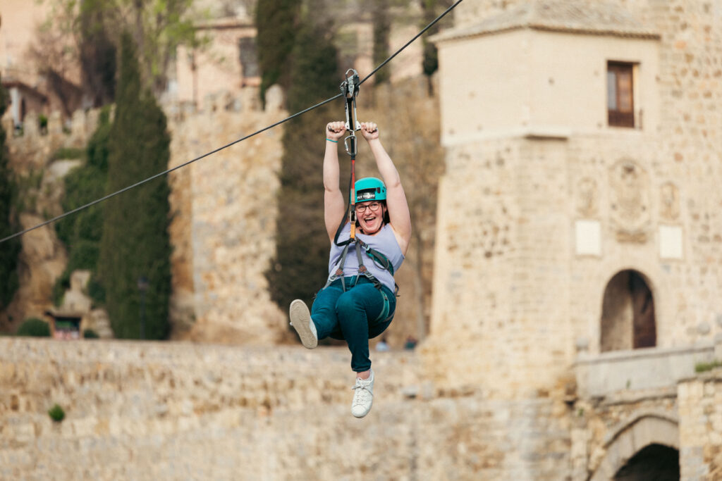 Woman on a zipline in Toledo, Spain wearing a blue helmet, purple tank top, and jeans