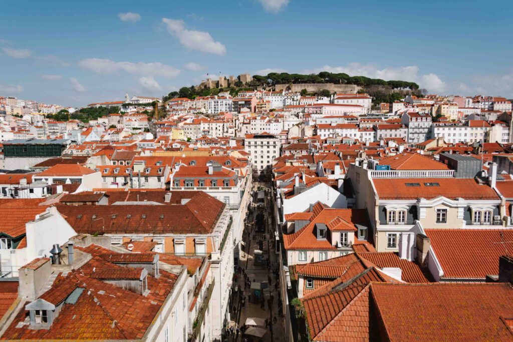 View of Lisbon from a high viewpoint in the city with orange and red thatched roofs and the castle on the far hill