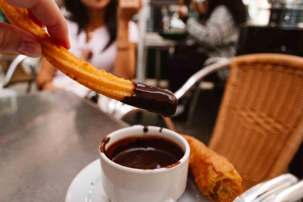 Churro dipped in chocolate in Madrid at an outdoor table