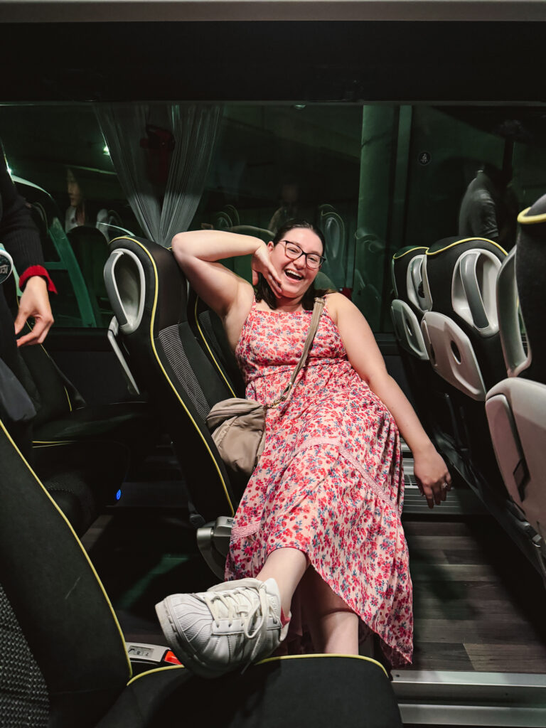 Woman lounging and sitting across two seats on a large coach bus with her feet in the aisle