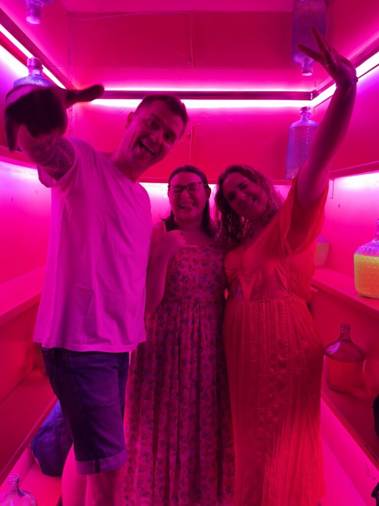 Three travelers posing for a fun photo in a bar in Madrid with bright pink lights.