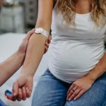 Pregnant woman in a exam room with bandage on her arm meant to indicate she has just had her blood drawn