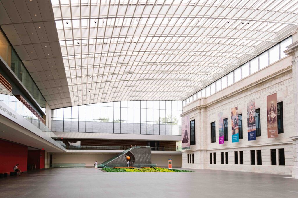 Interior lobby atrium of Cleveland Museum of Art with tall glass ceiling and exhibits to the left and right