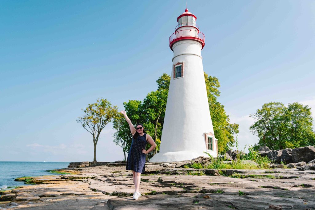Woman in a blue polka dotted dress posing in front of a white and red lighthouse on the shores of Ohio Lake Erie