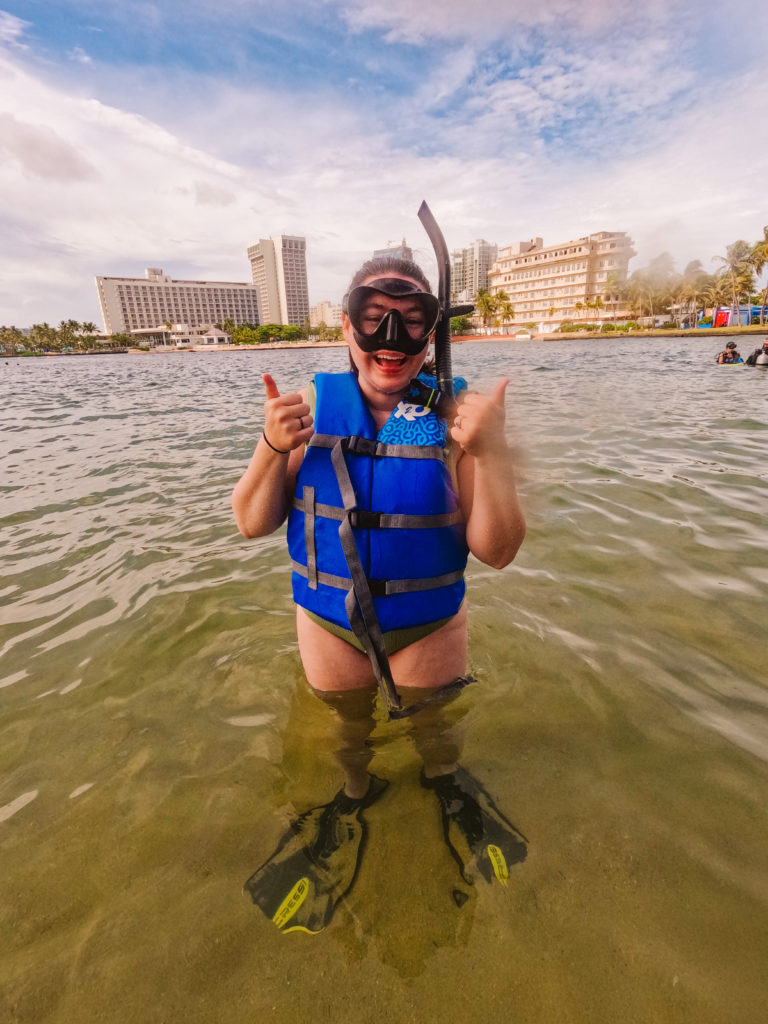 Woman smiling wearing snorkeling gear standing thigh deep in the ocean
